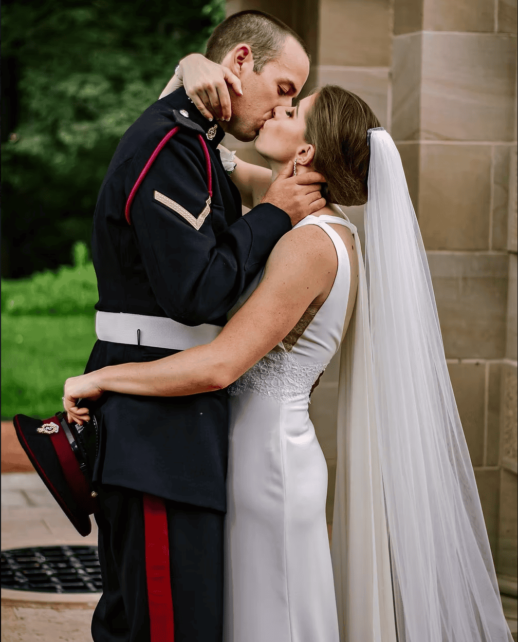 Military groom kisses bride against a sandstone pillar